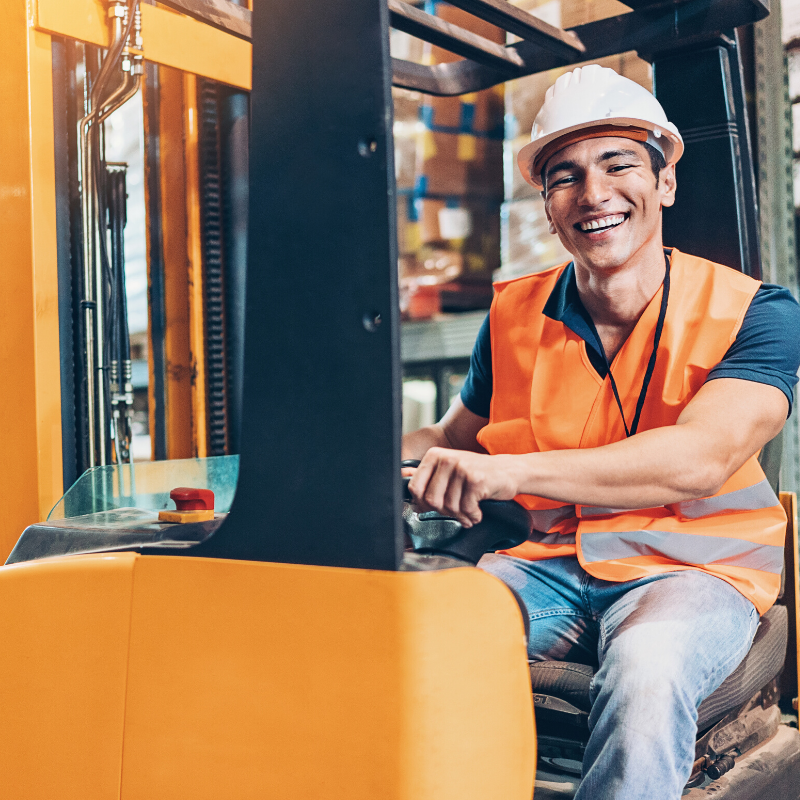 Man wearing a construction hard hat and driving a forklift in a warehouse
